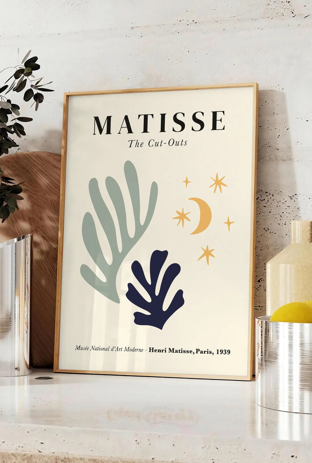 Affiche corail Lune et Etoiles en papiers decoupes Matisse sur fond colore, posee sur un plan de travail de cuisine en pierre claire, entre une branche d'eucalyptus en vase et un bocal de citrons