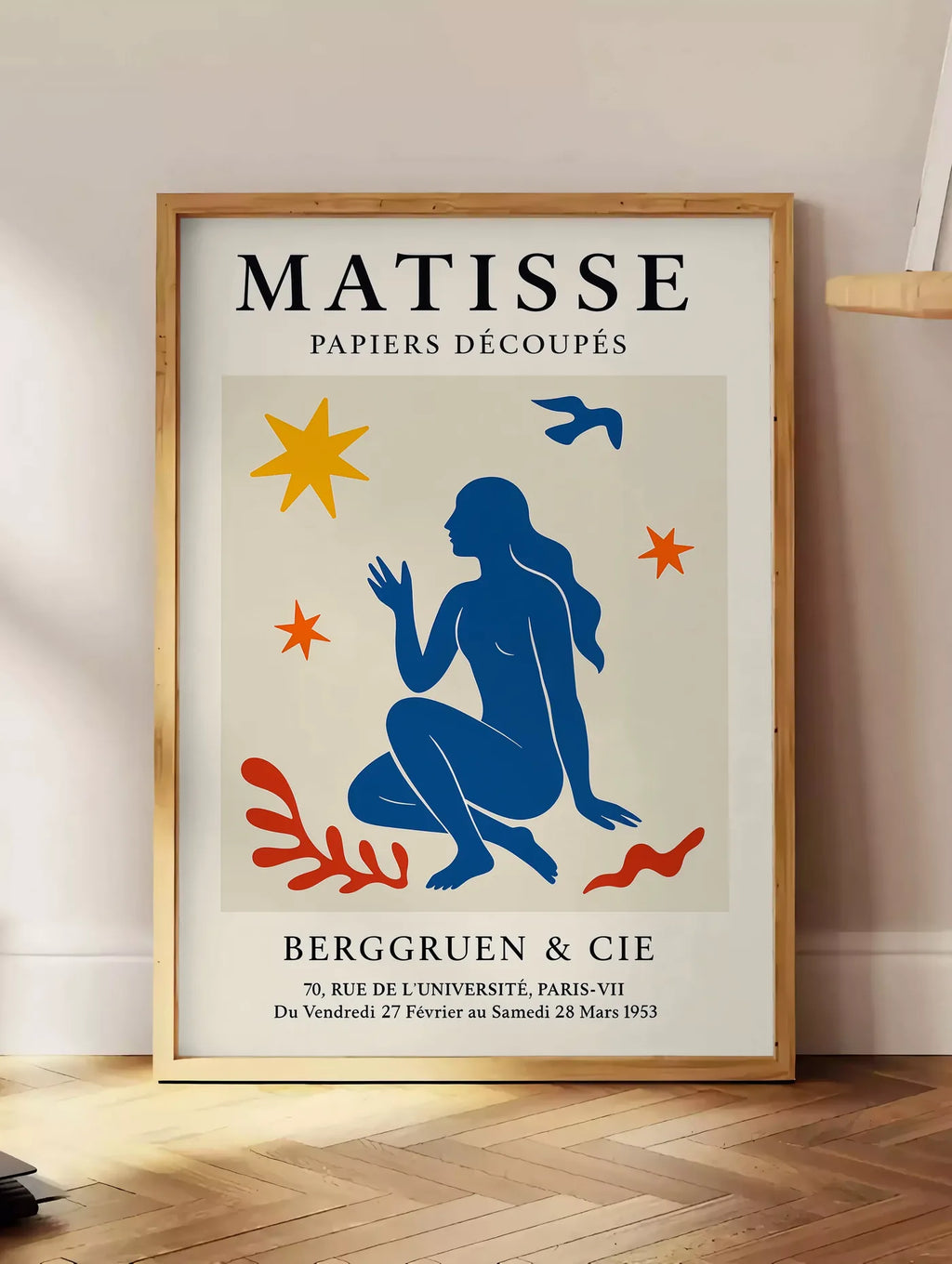 Estampe femme bleue parmi etoiles et un oiseau, posee au sol dans un coin salon, sur un parquet a chevrons, pres d'une table d'appoint en chene chargee de livres