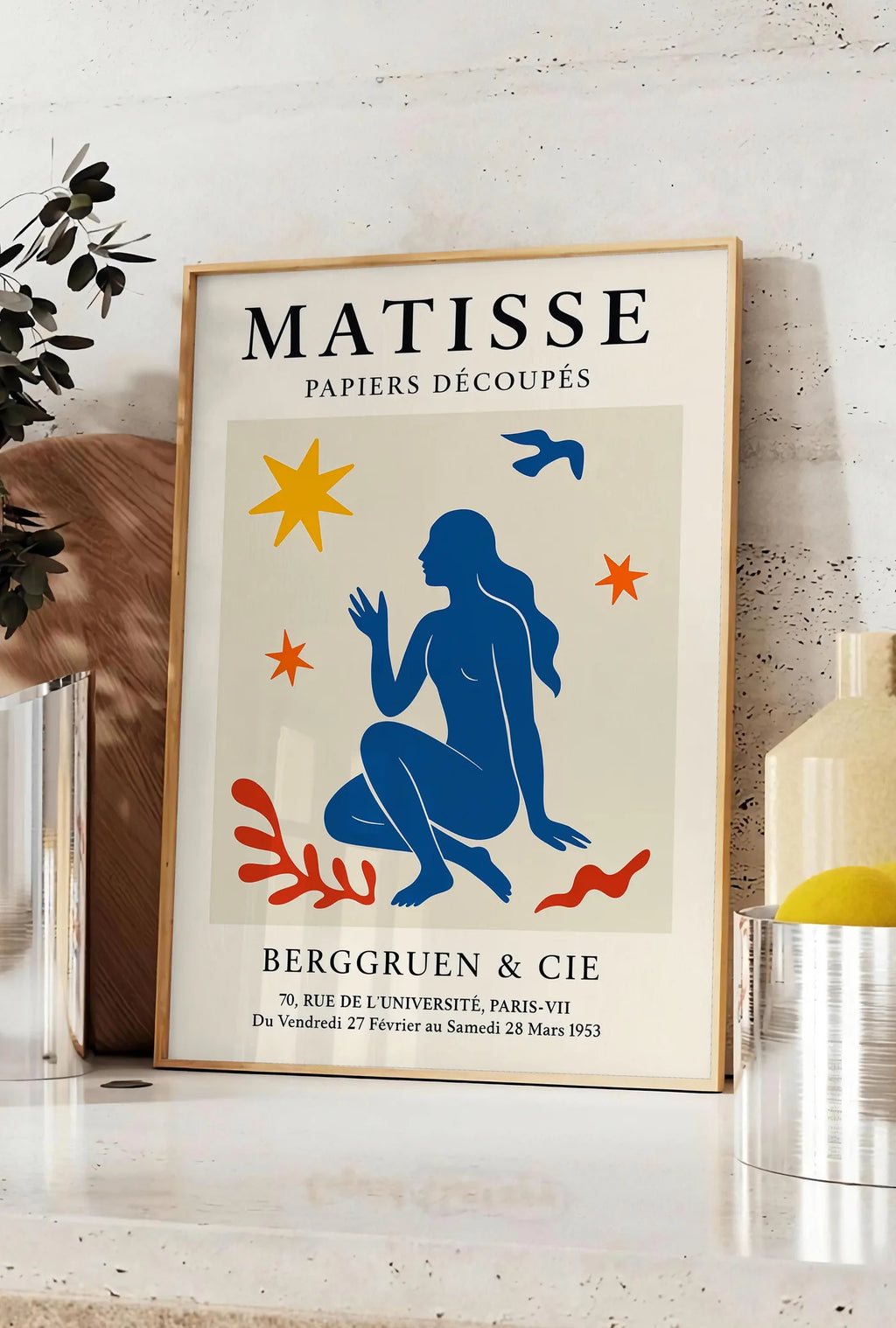 Affiche femme bleue parmi etoiles et un oiseau, posee sur un plan de travail de cuisine en pierre claire, entre une branche d'eucalyptus en vase et un bocal de citrons