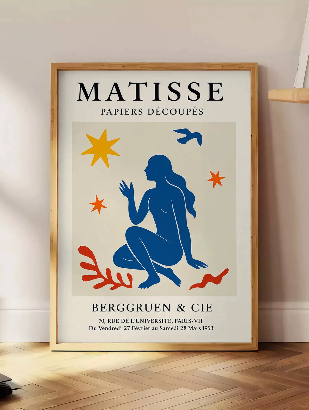 Estampe femme bleue parmi etoiles et un oiseau, posee au sol dans un coin salon, sur un parquet a chevrons, pres d'une table d'appoint en chene chargee de livres