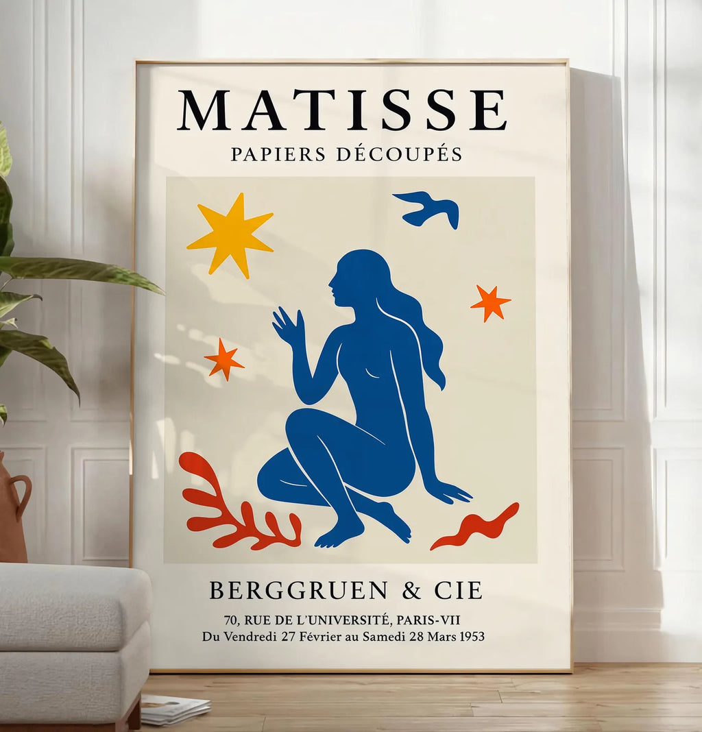 Reproduction femme bleue parmi etoiles et un oiseau, posee au sol dans un salon minimaliste clair, a cote d'un canape beige et d'une plante verte, sur un parquet clair