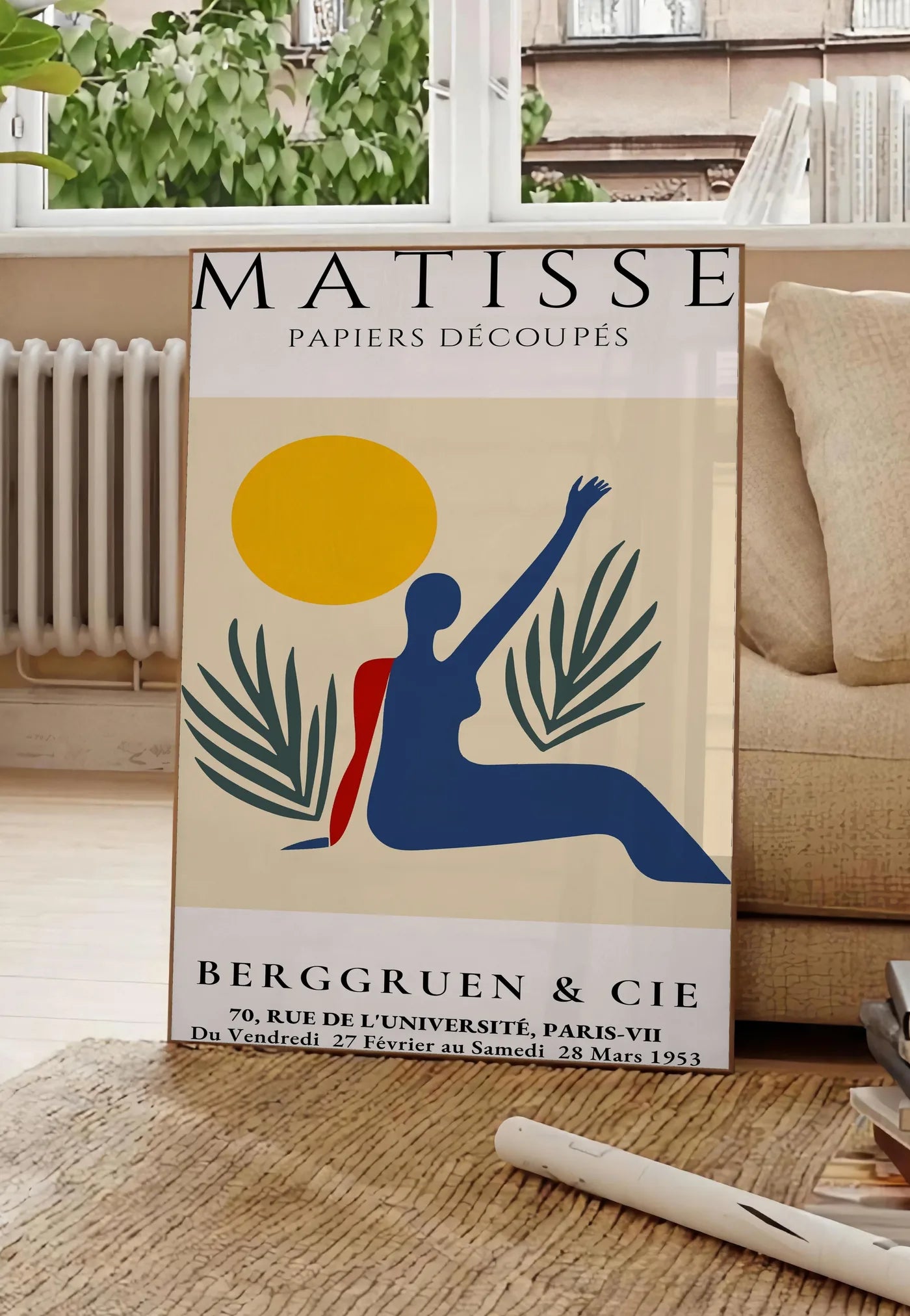 Poster femme bleue au bras leve sous un soleil jaune et des palmes, posee au sol dans un salon parisien, devant une grande fenetre donnant sur un immeuble haussmannien, entre un ficus et un canape creme