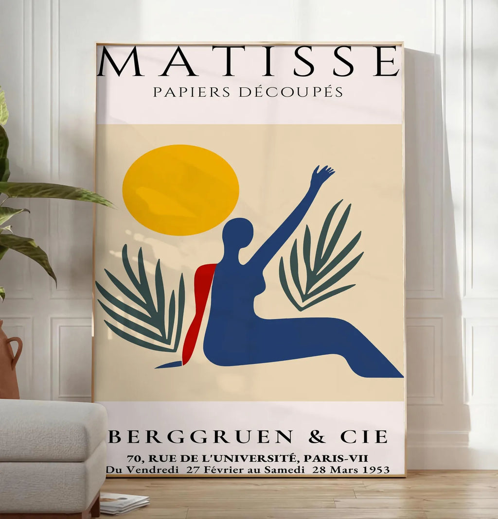 Reproduction femme bleue au bras leve sous un soleil jaune et des palmes, posee au sol dans un salon minimaliste clair, a cote d'un canape beige et d'une plante verte, sur un parquet clair