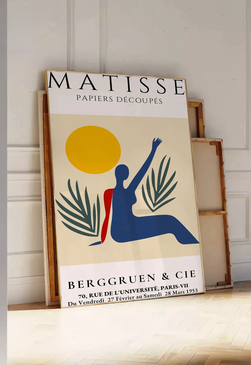 Tirage encadrable femme bleue au bras leve sous un soleil jaune et des palmes, posee au sol dans une entree lumineuse, contre un mur a panneaux blancs, a cote de chassis en bois empiles