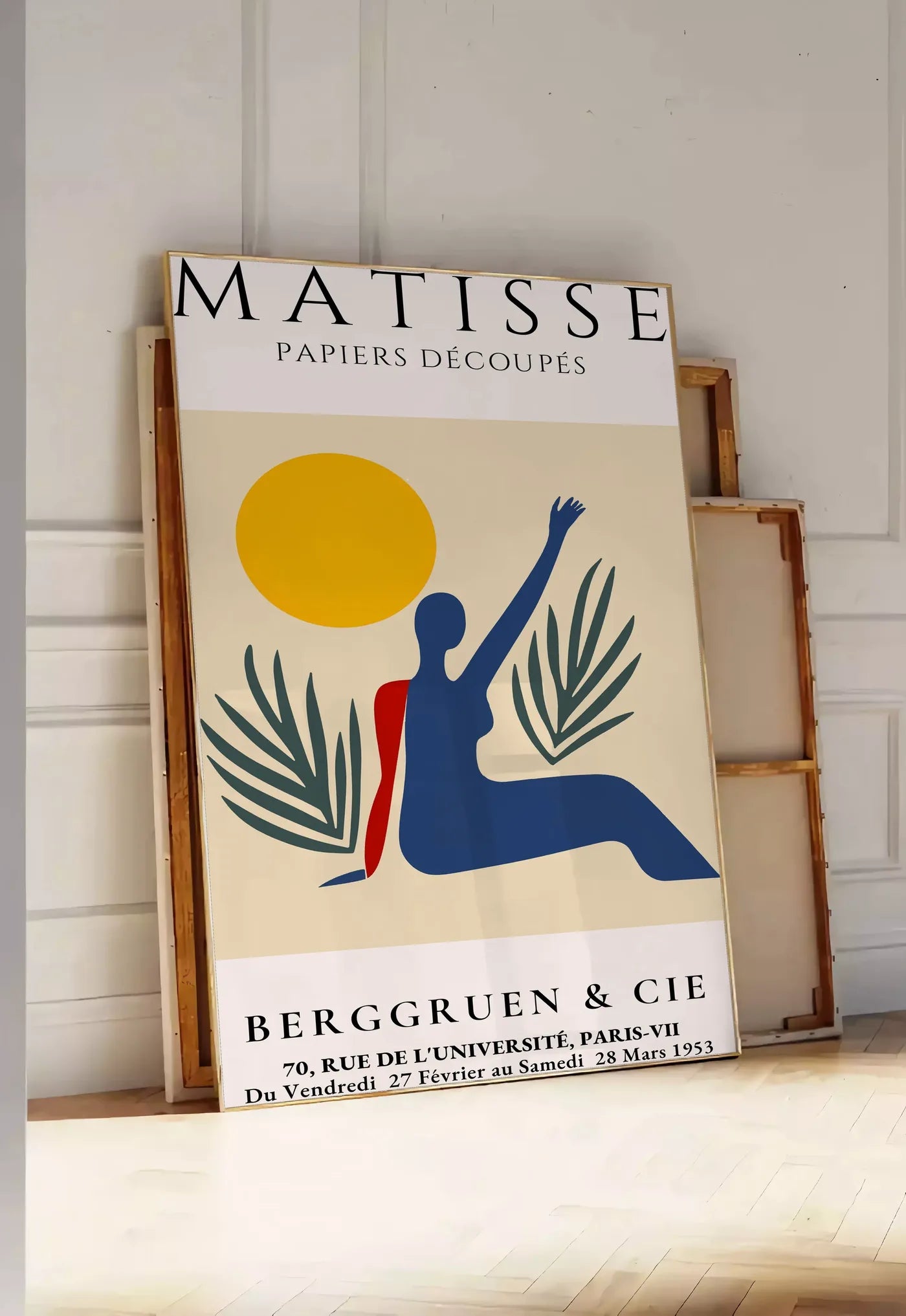 Tirage encadrable femme bleue au bras leve sous un soleil jaune et des palmes, posee au sol dans une entree lumineuse, contre un mur a panneaux blancs, a cote de chassis en bois empiles