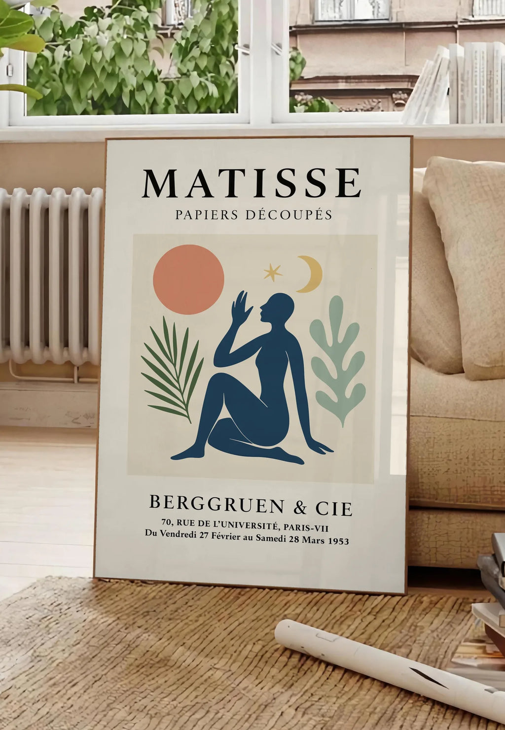 Poster femme bleue avec lune croissant et etoile, posee au sol dans un salon parisien, devant une grande fenetre donnant sur un immeuble haussmannien, entre un ficus et un canape creme