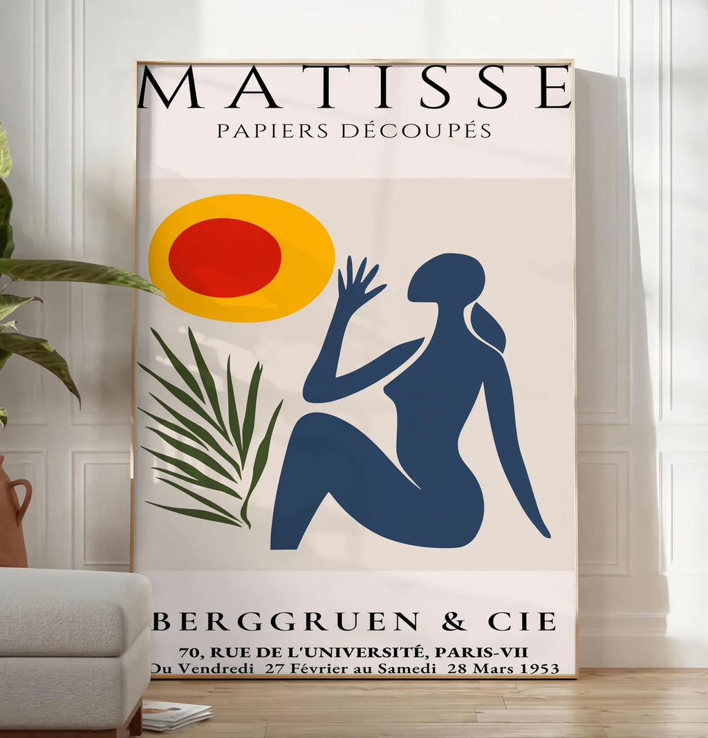 Reproduction femme bleue tendue vers un soleil rouge et jaune et une palme, posee au sol dans un salon minimaliste clair, a cote d'un canape beige et d'une plante verte, sur un parquet clair