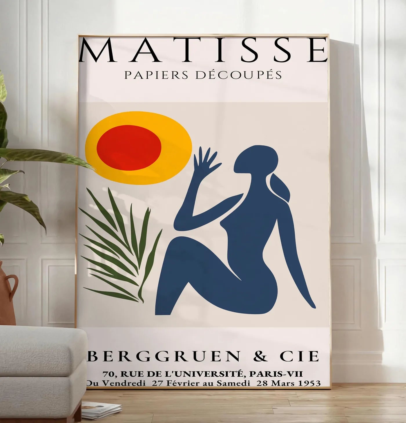 Reproduction femme bleue tendue vers un soleil rouge et jaune et une palme, posee au sol dans un salon minimaliste clair, a cote d'un canape beige et d'une plante verte, sur un parquet clair