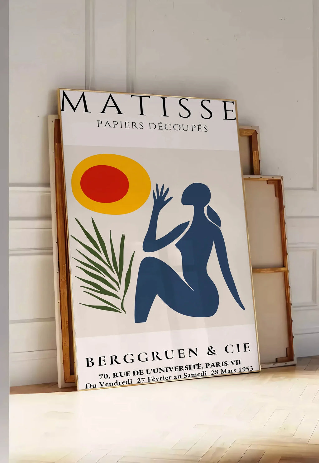 Tirage encadrable femme bleue tendue vers un soleil rouge et jaune et une palme, posee au sol dans une entree lumineuse, contre un mur a panneaux blancs, a cote de chassis en bois empiles