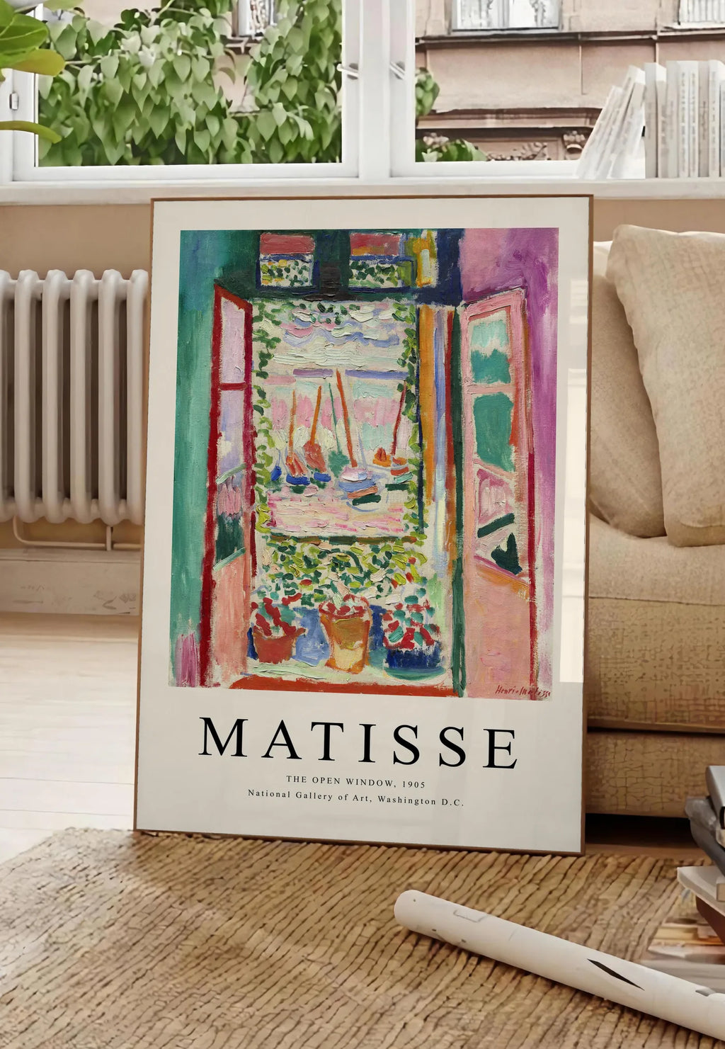 Poster fenetre ouverte sur une mer rose et turquoise aux voiliers, posee au sol dans un salon parisien, devant une grande fenetre donnant sur un immeuble haussmannien, entre un ficus et un canape creme