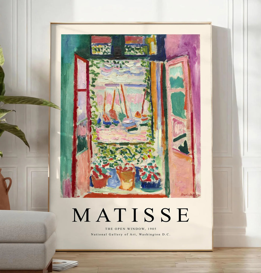 Reproduction fenetre ouverte sur une mer rose et turquoise aux voiliers, posee au sol dans un salon minimaliste clair, a cote d'un canape beige et d'une plante verte, sur un parquet clair