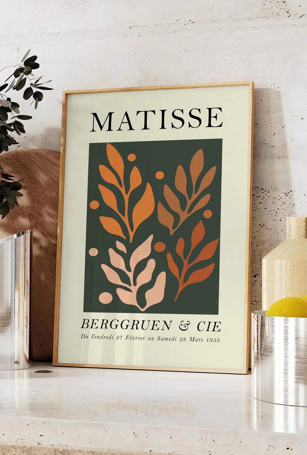 Affiche feuillages Orange sur Vert en papiers decoupes Matisse sur fond colore, posee sur un plan de travail de cuisine en pierre claire, entre une branche d'eucalyptus en vase et un bocal de citrons
