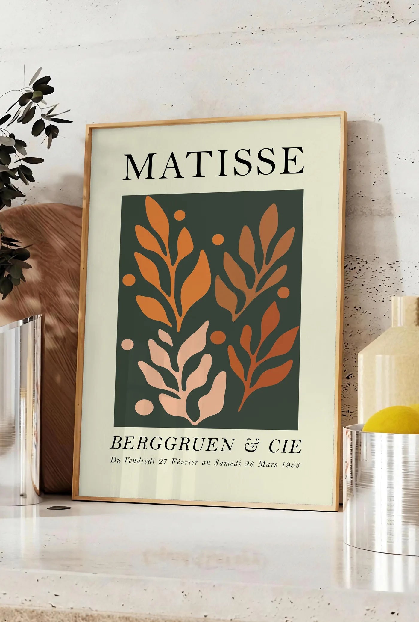 Affiche feuillages Orange sur Vert en papiers decoupes Matisse sur fond colore, posee sur un plan de travail de cuisine en pierre claire, entre une branche d'eucalyptus en vase et un bocal de citrons