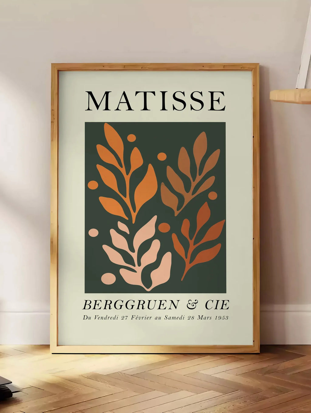 Estampe feuillages Orange sur Vert en papiers decoupes Matisse sur fond colore, posee au sol dans un coin salon, sur un parquet a chevrons, pres d'une table d'appoint en chene chargee de livres