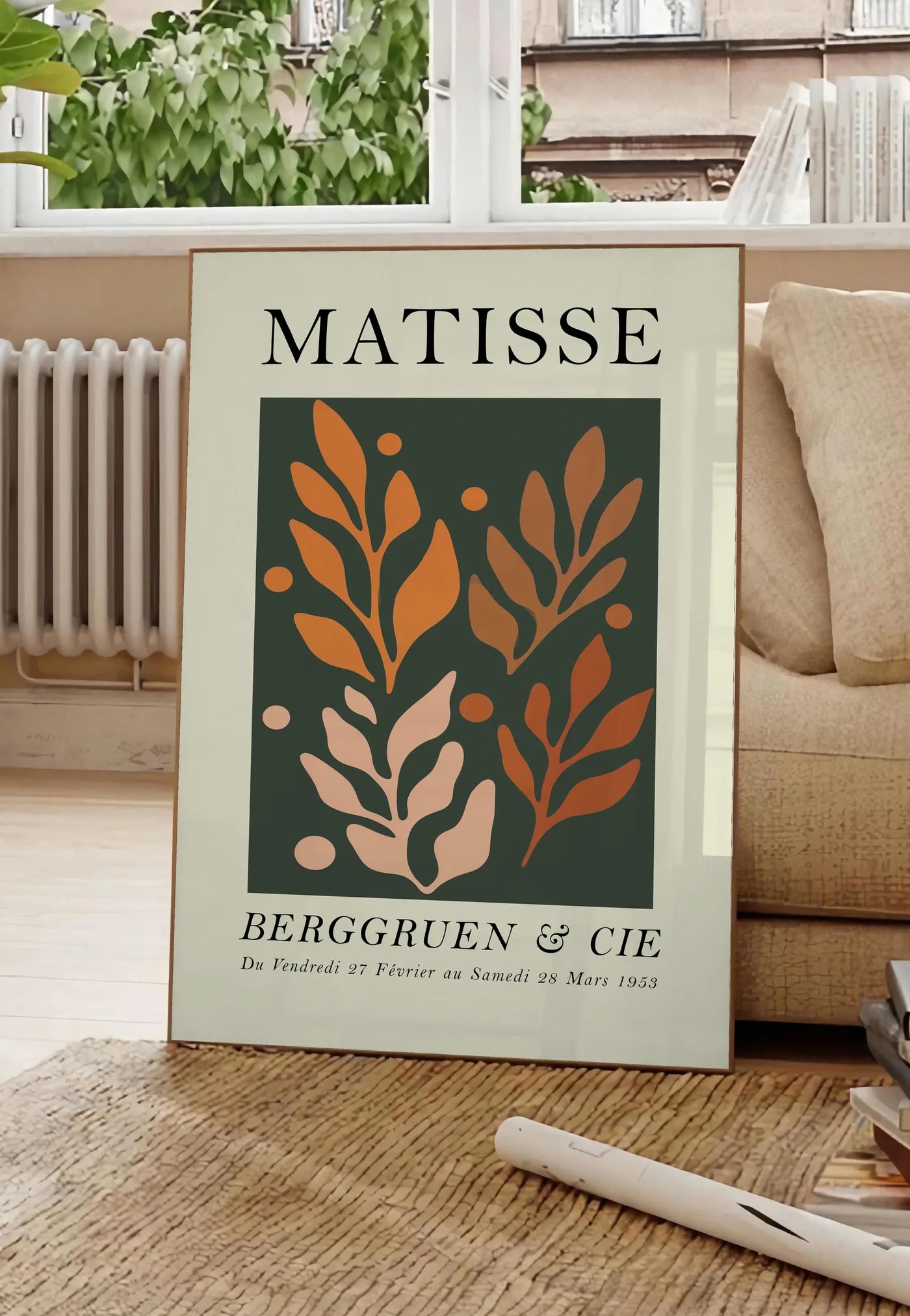Poster feuillages Orange sur Vert en papiers decoupes Matisse sur fond colore, posee au sol dans un salon parisien, devant une grande fenetre donnant sur un immeuble haussmannien, entre un ficus et un canape creme