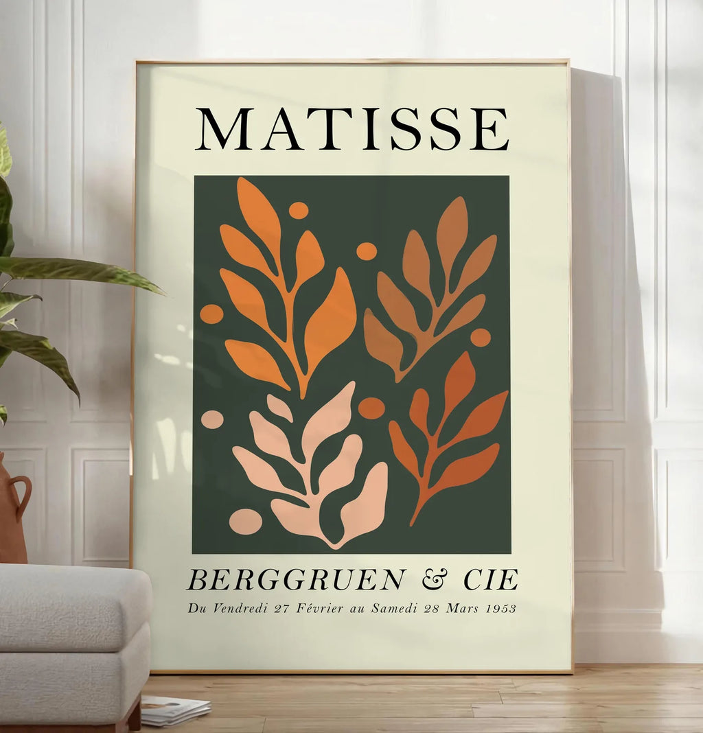 Reproduction feuillages Orange sur Vert en papiers decoupes Matisse sur fond colore, posee au sol dans un salon minimaliste clair, a cote d'un canape beige et d'une plante verte, sur un parquet clair