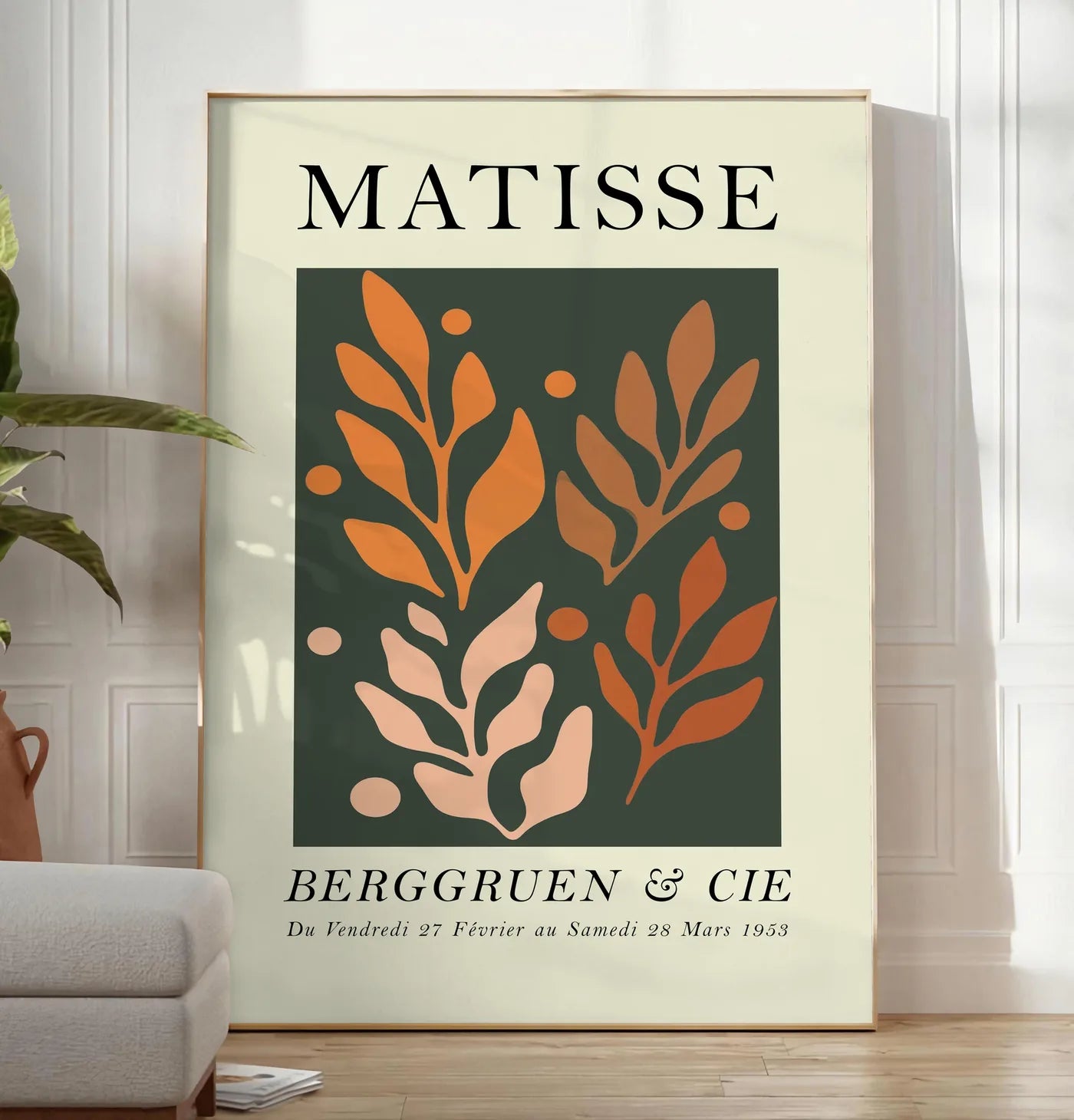Reproduction feuillages Orange sur Vert en papiers decoupes Matisse sur fond colore, posee au sol dans un salon minimaliste clair, a cote d'un canape beige et d'une plante verte, sur un parquet clair
