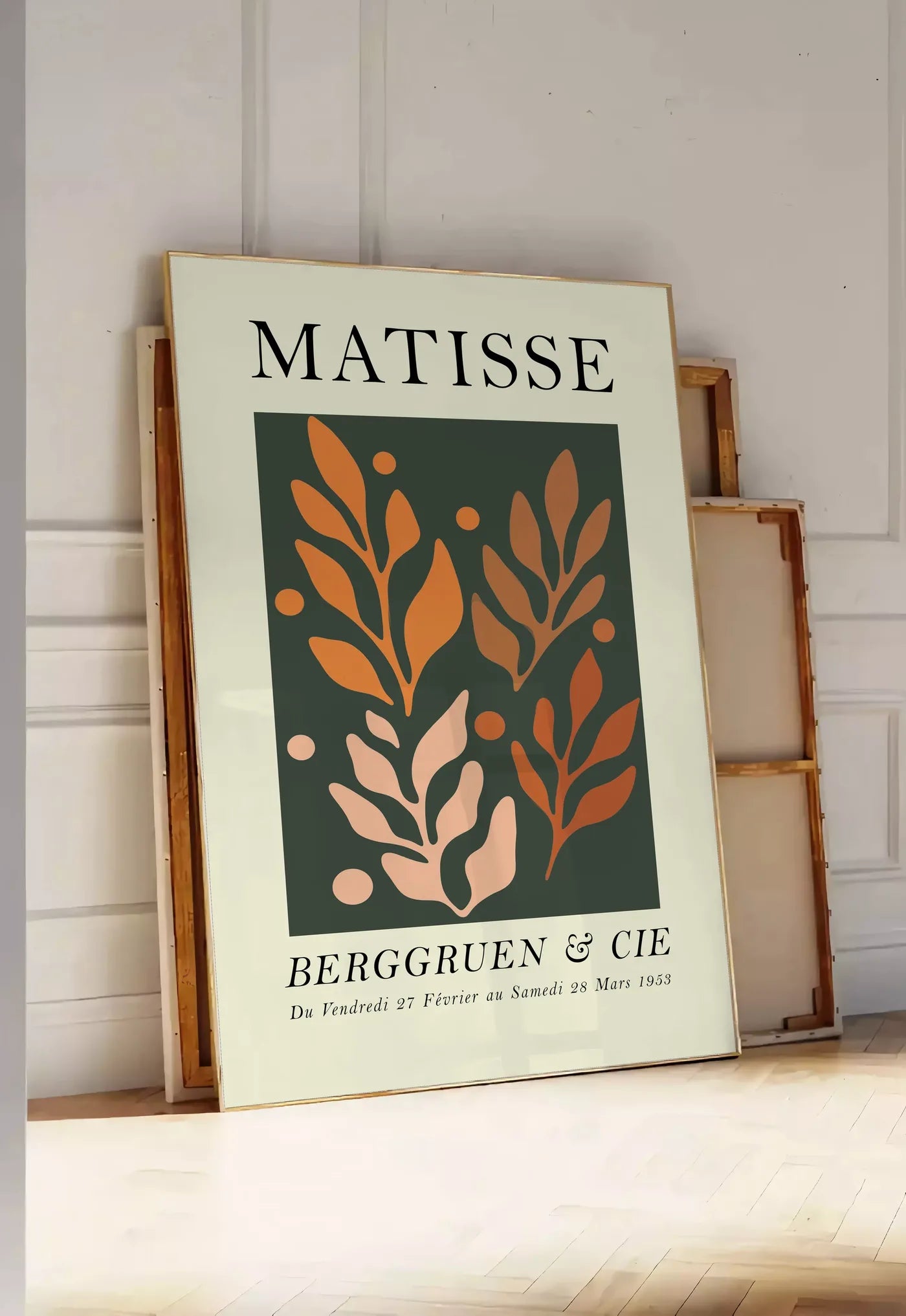 Tirage encadrable feuillages Orange sur Vert en papiers decoupes Matisse sur fond colore, posee au sol dans une entree lumineuse, contre un mur a panneaux blancs, a cote de chassis en bois empiles