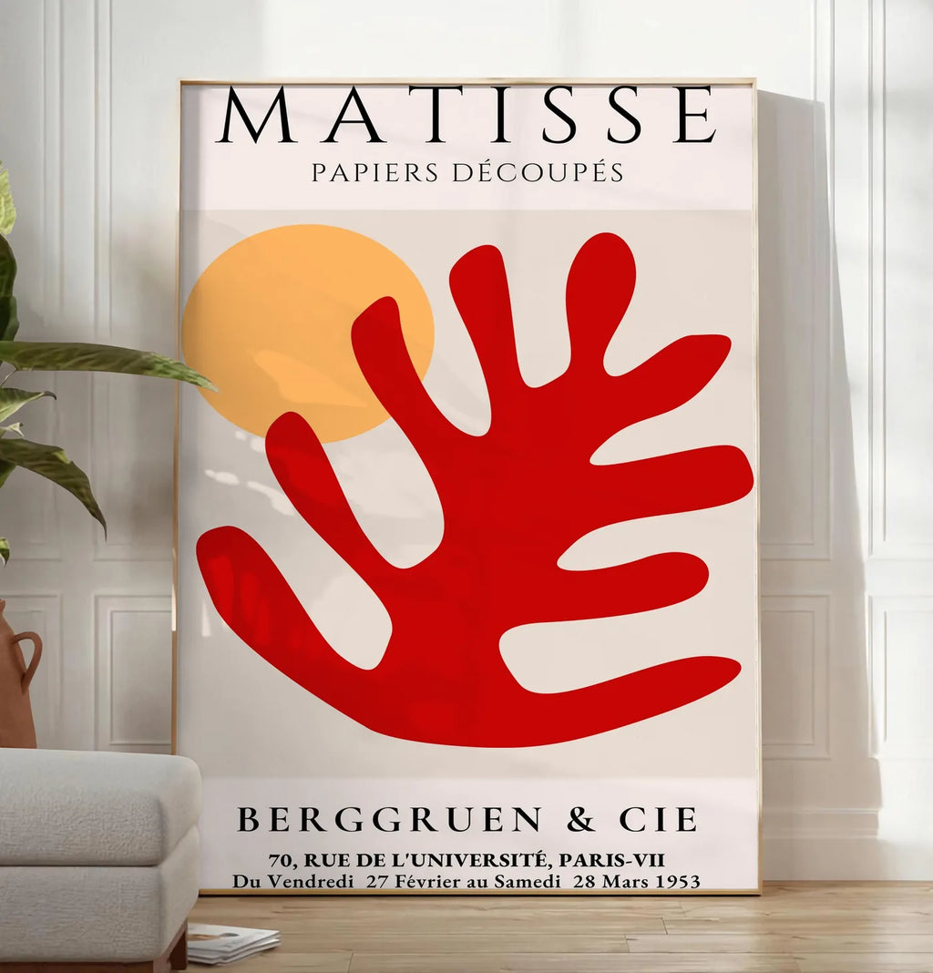 Reproduction feuille corail rouge et soleil orange sur fond creme, posee au sol dans un salon minimaliste clair, a cote d'un canape beige et d'une plante verte, sur un parquet clair