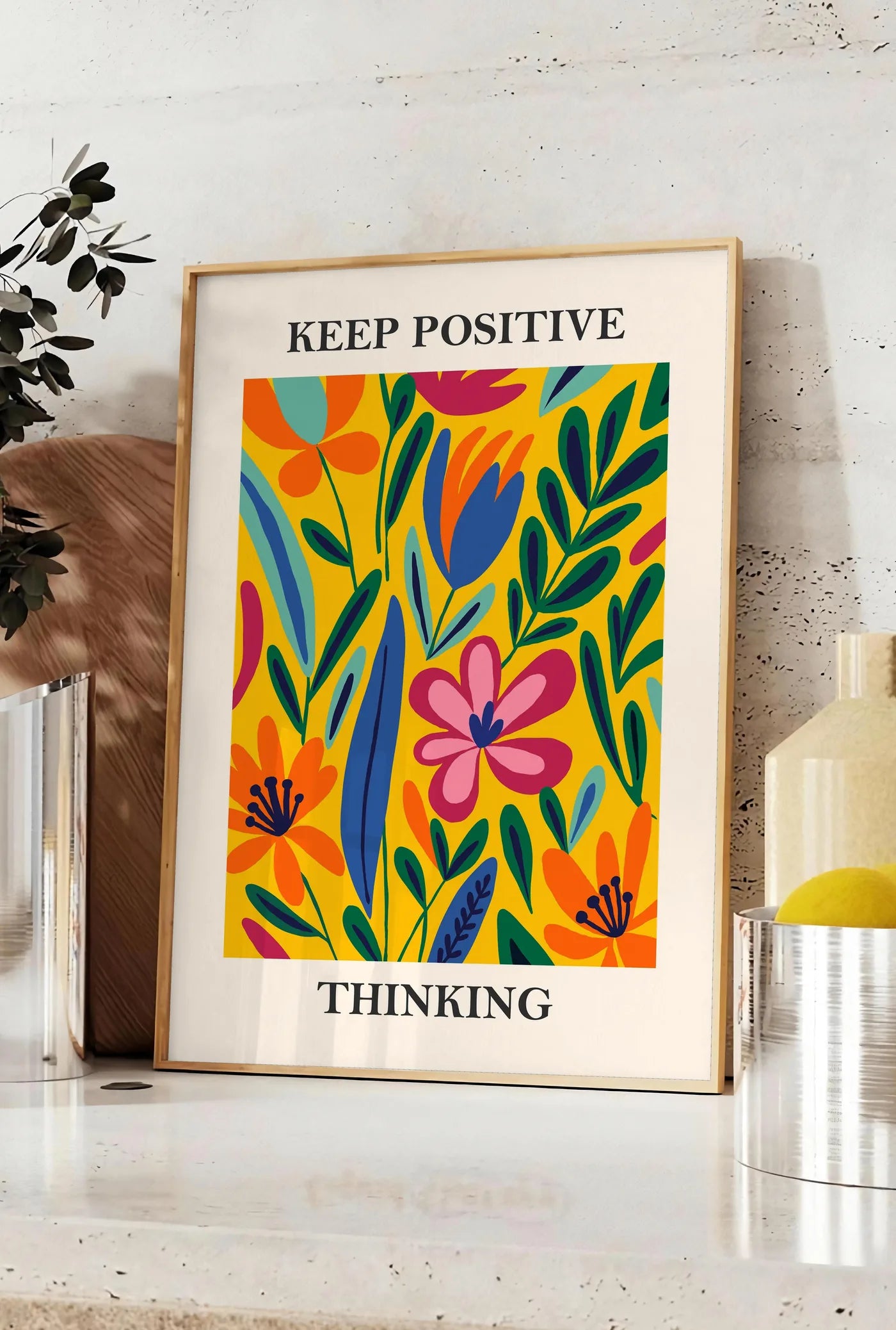Affiche fleurs maximalistes colorees sur fond jaune, posee sur un plan de travail de cuisine en pierre claire, entre une branche d'eucalyptus en vase et un bocal de citrons