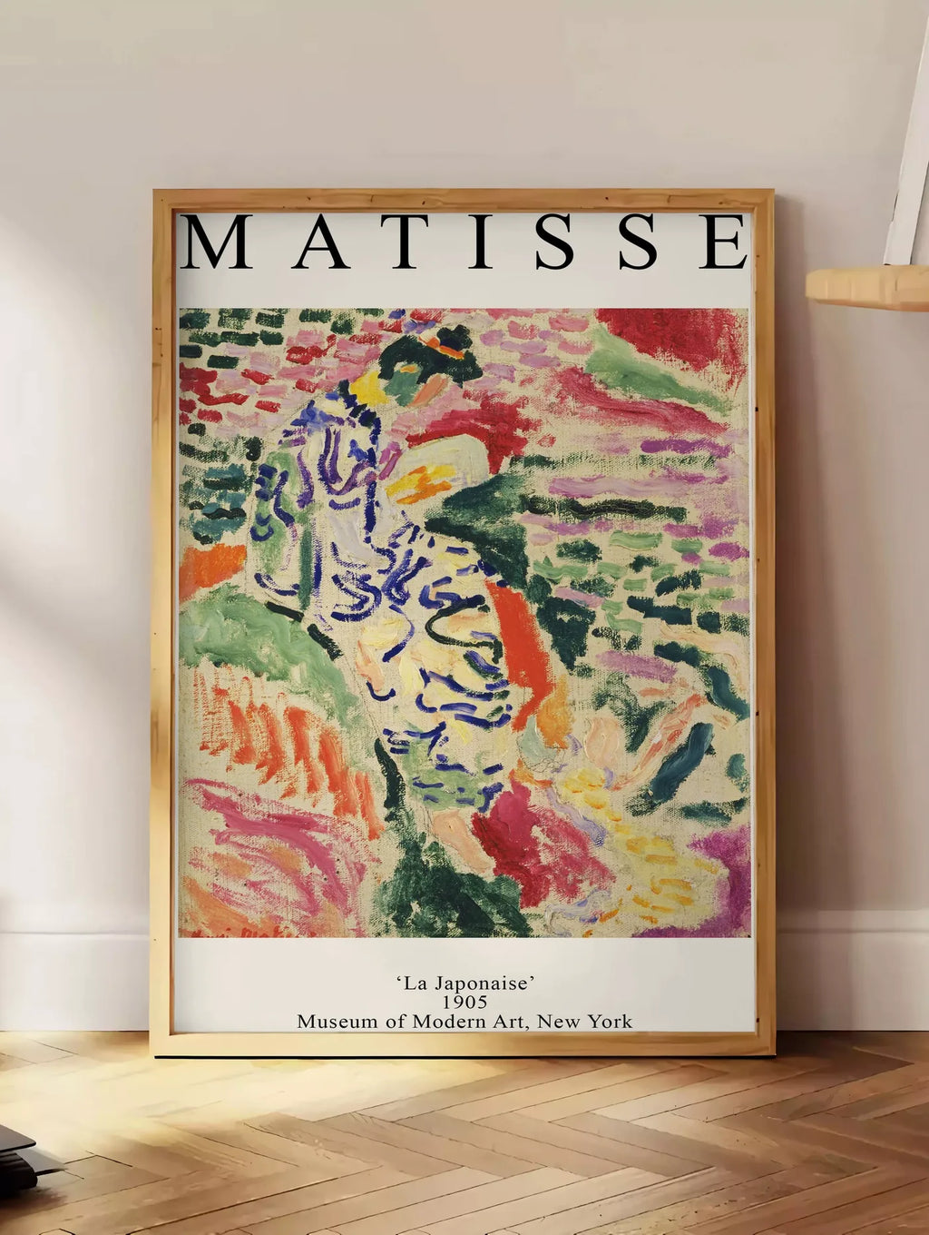 Estampe matisse La Japonaise 1905, posee au sol dans un coin salon, sur un parquet a chevrons, pres d'une table d'appoint en chene chargee de livres