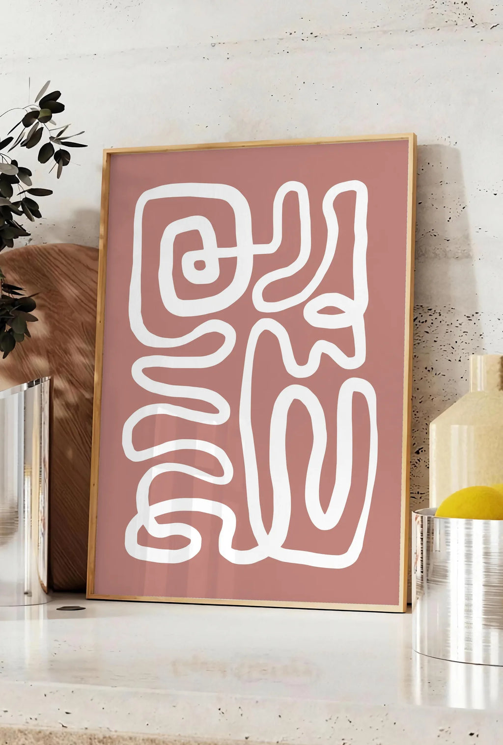Affiche ligne continue blanche abstraite sur fond terracotta, posee sur un plan de travail de cuisine en pierre claire, entre une branche d'eucalyptus en vase et un bocal de citrons