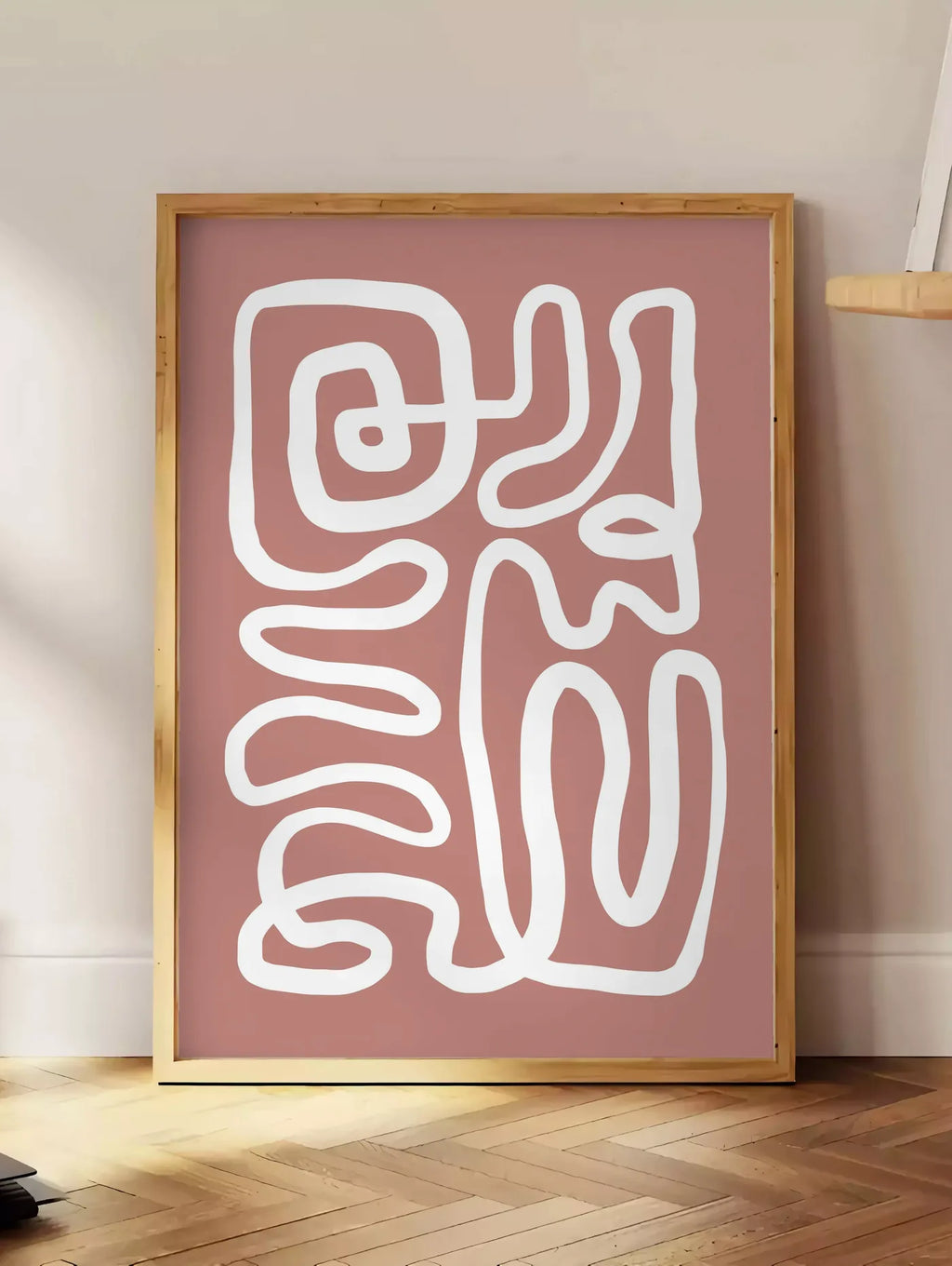 Estampe ligne continue blanche abstraite sur fond terracotta, posee au sol dans un coin salon, sur un parquet a chevrons, pres d'une table d'appoint en chene chargee de livres