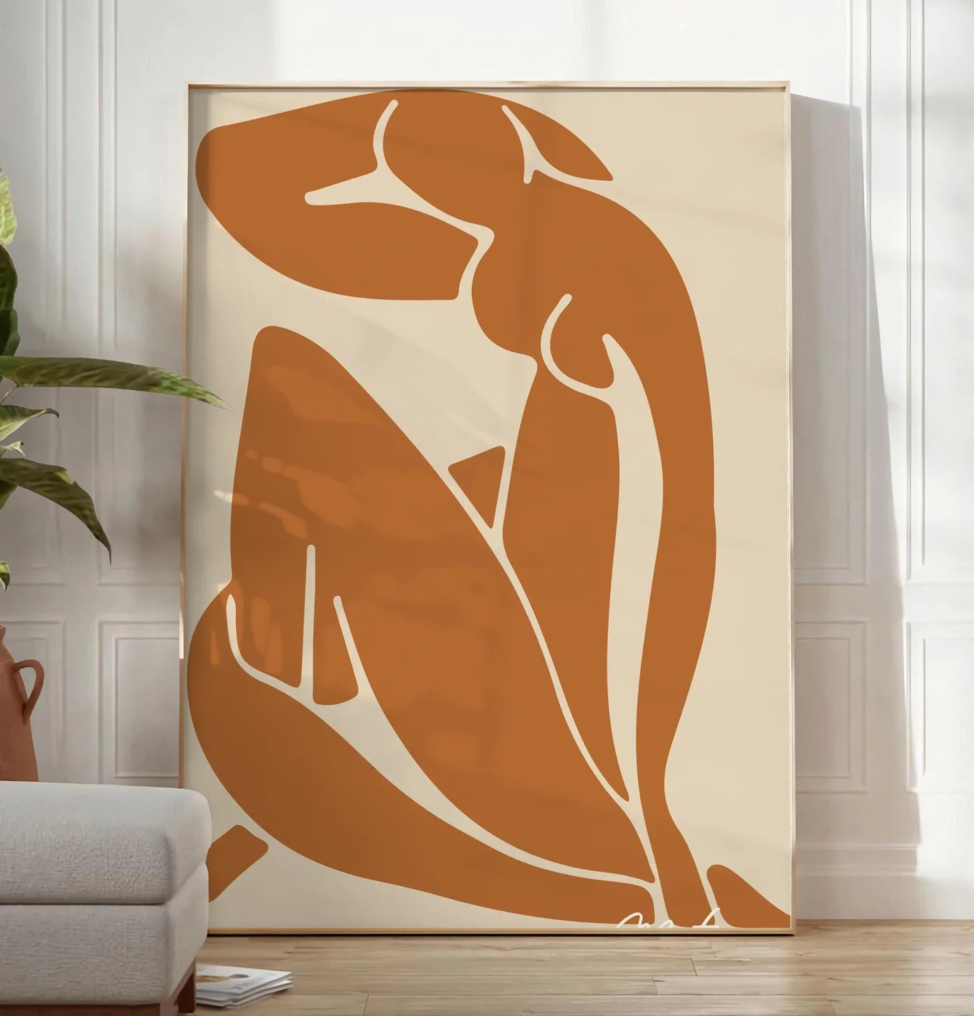 Reproduction silhouette nue découpée terracotta sur fond beige, posee au sol dans un salon minimaliste clair, a cote d'un canape beige et d'une plante verte, sur un parquet clair