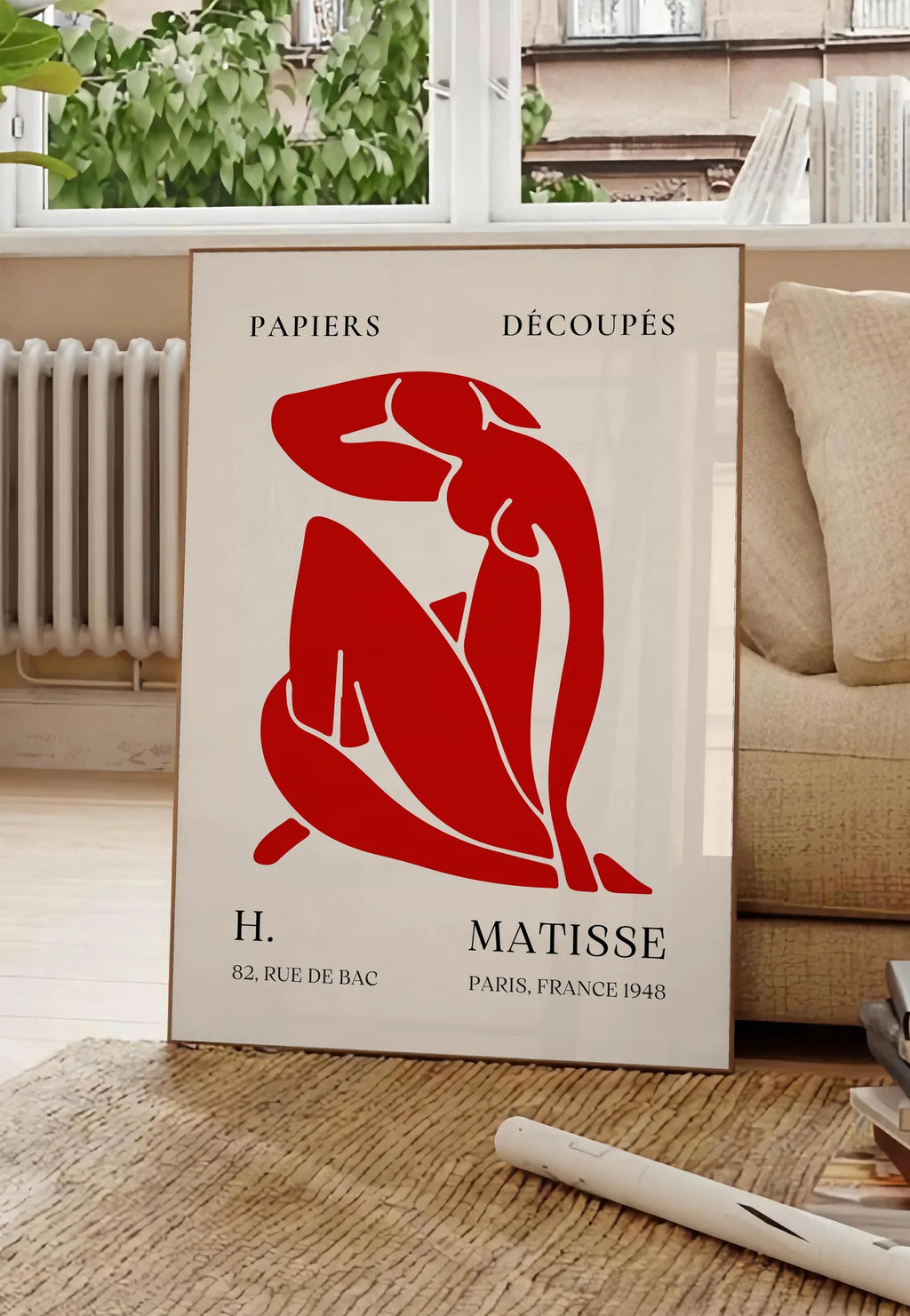 Poster affiche Matisse Papiers Decoupes, posee au sol dans un salon parisien, devant une grande fenetre donnant sur un immeuble haussmannien, entre un ficus et un canape creme