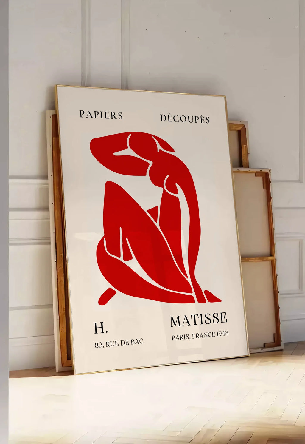 Tirage encadrable affiche Matisse Papiers Decoupes, posee au sol dans une entree lumineuse, contre un mur a panneaux blancs, a cote de chassis en bois empiles