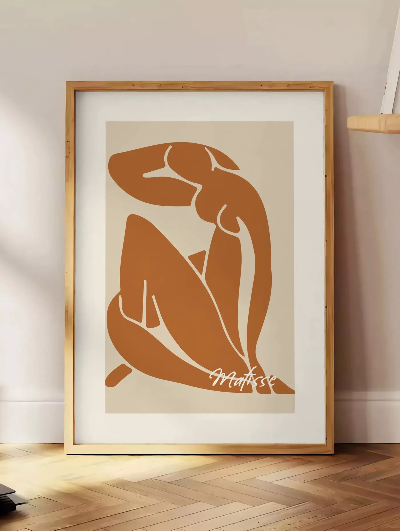 Estampe affiche Matisse, posee au sol dans un coin salon, sur un parquet a chevrons, pres d'une table d'appoint en chene chargee de livres