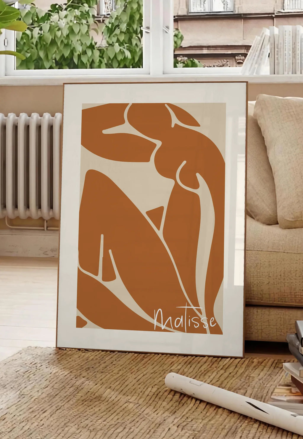 Poster nu assis terracotta au trait blanc sur fond creme, posee au sol dans un salon parisien, devant une grande fenetre donnant sur un immeuble haussmannien, entre un ficus et un canape creme