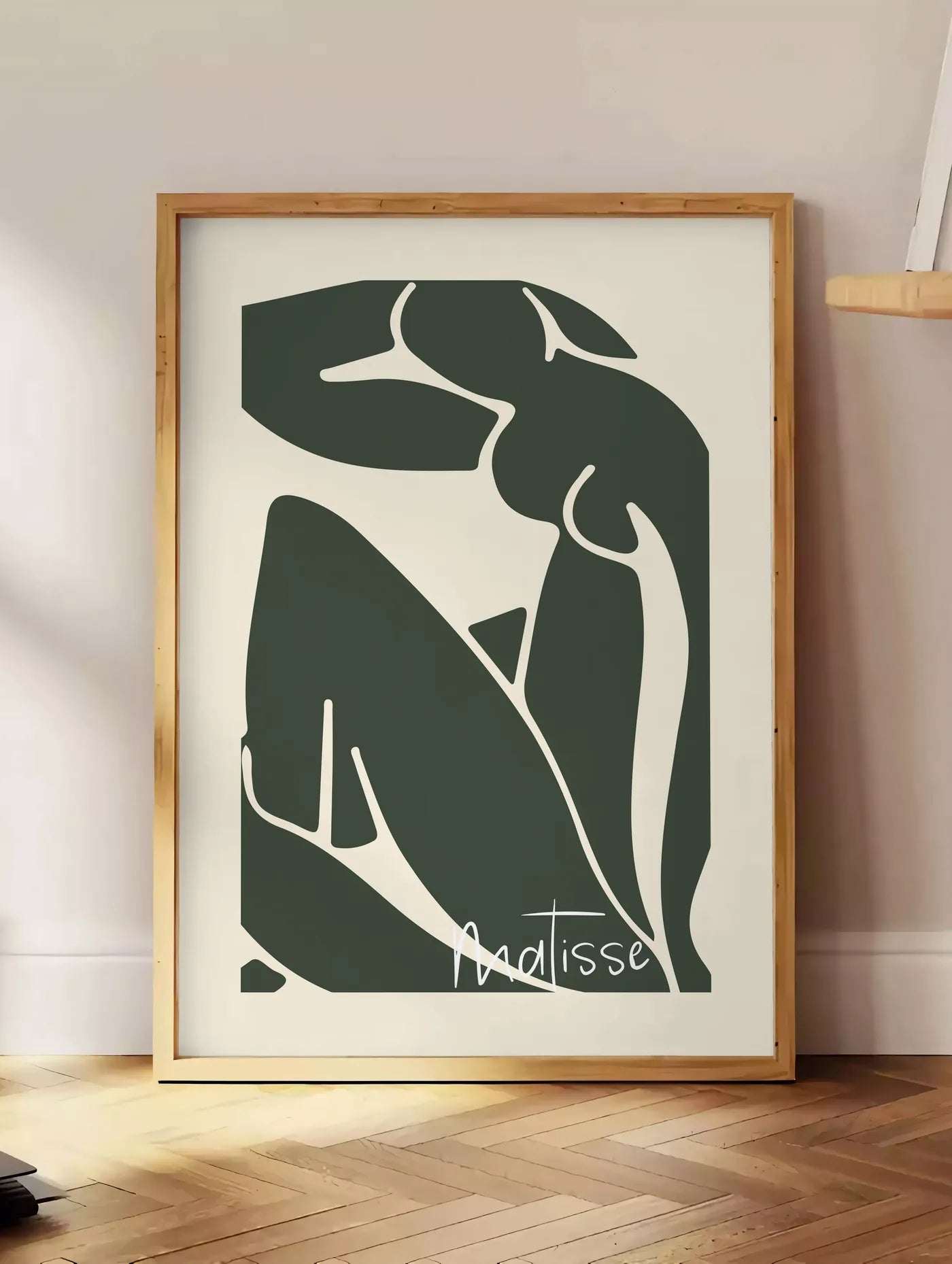 Estampe nu assis vert au trait blanc sur fond creme, posee au sol dans un coin salon, sur un parquet a chevrons, pres d'une table d'appoint en chene chargee de livres