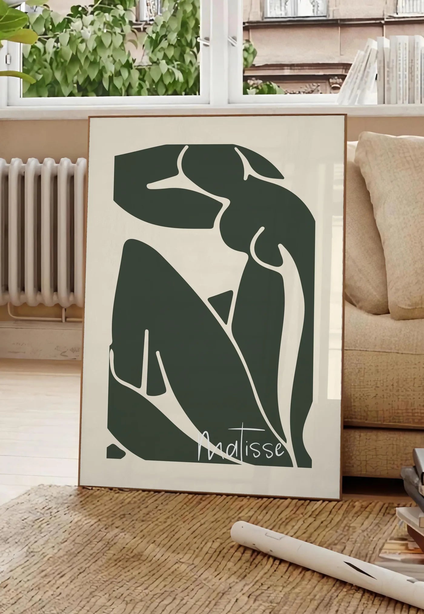Poster nu assis vert au trait blanc sur fond creme, posee au sol dans un salon parisien, devant une grande fenetre donnant sur un immeuble haussmannien, entre un ficus et un canape creme