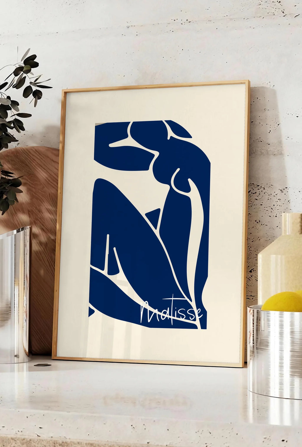 Affiche image de silhouette de femme assise en formes découpées bleu de cobalt sur fond blanc cassé, posee sur un plan de travail de cuisine en pierre claire, entre une branche d'eucalyptus en vase et un bocal de citrons