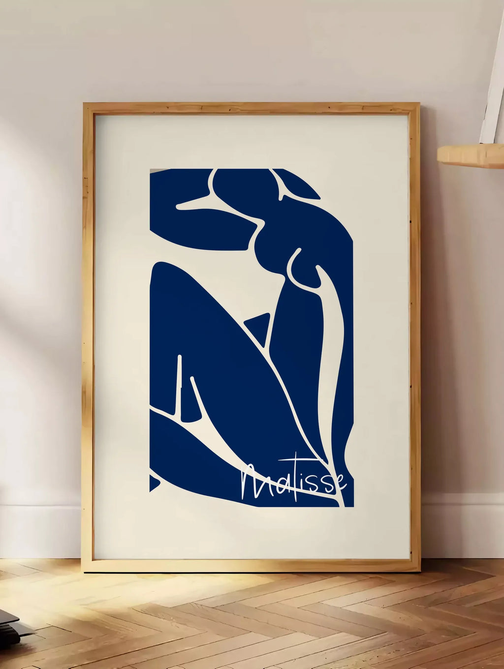 Estampe image de silhouette de femme assise en formes découpées bleu de cobalt sur fond blanc cassé, posee au sol dans un coin salon, sur un parquet a chevrons, pres d'une table d'appoint en chene chargee de livres