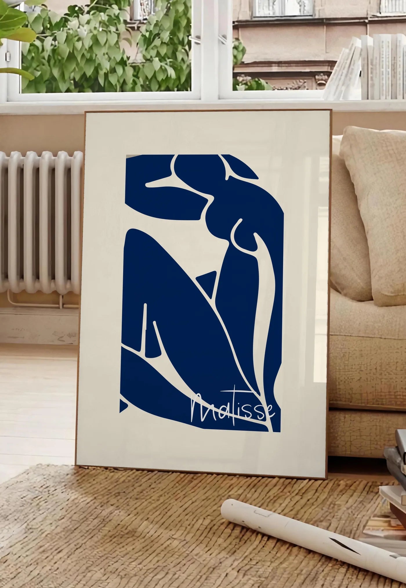 Poster image de silhouette de femme assise en formes découpées bleu de cobalt sur fond blanc cassé, posee au sol dans un salon parisien, devant une grande fenetre donnant sur un immeuble haussmannien, entre un ficus et un canape creme