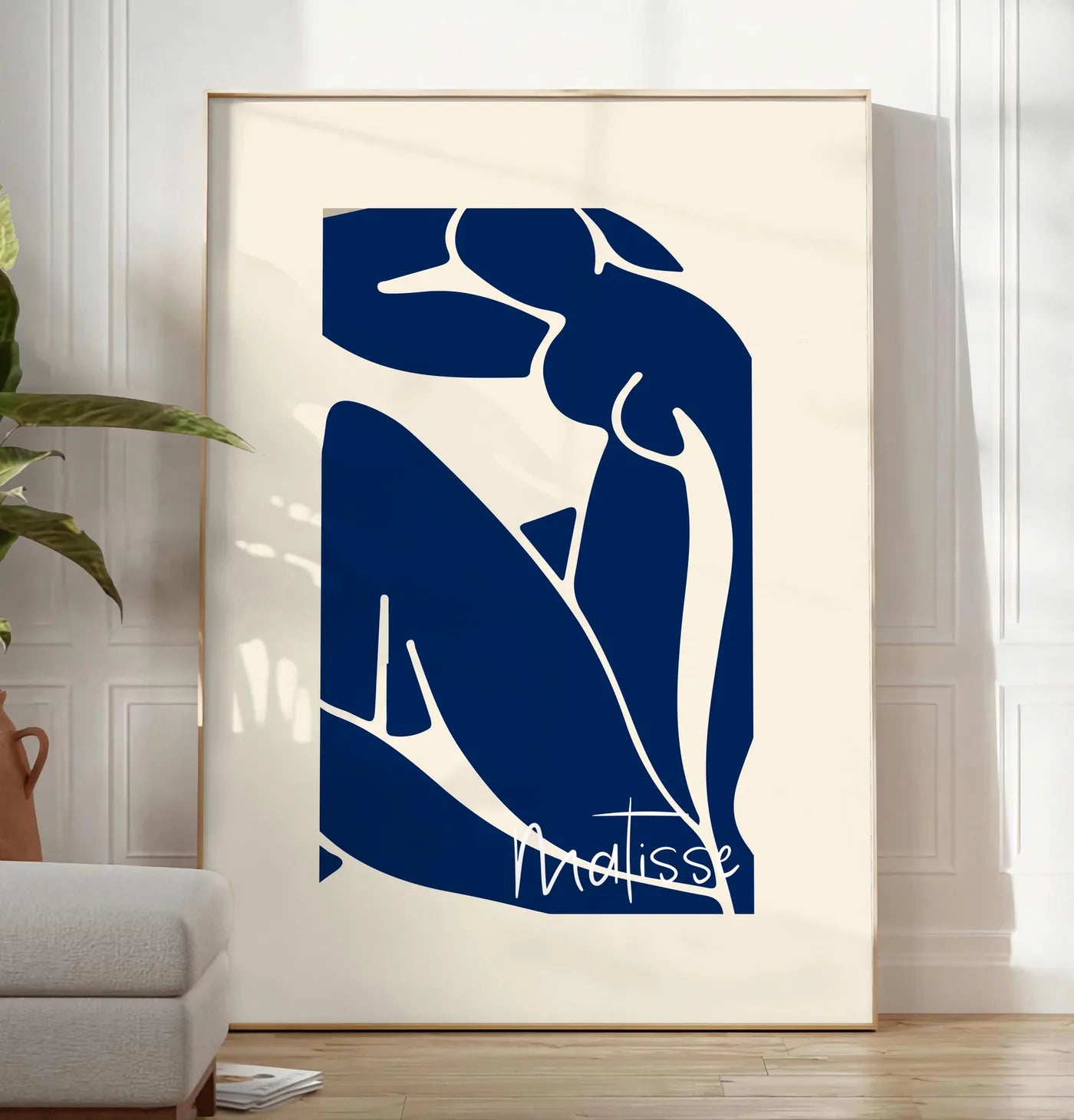 Reproduction image de silhouette de femme assise en formes découpées bleu de cobalt sur fond blanc cassé, posee au sol dans un salon minimaliste clair, a cote d'un canape beige et d'une plante verte, sur un parquet clair