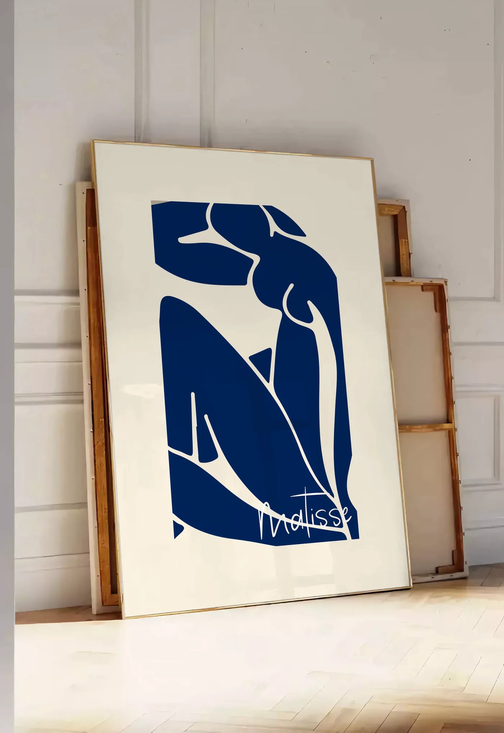 Tirage encadrable image de silhouette de femme assise en formes découpées bleu de cobalt sur fond blanc cassé, posee au sol dans une entree lumineuse, contre un mur a panneaux blancs, a cote de chassis en bois empiles