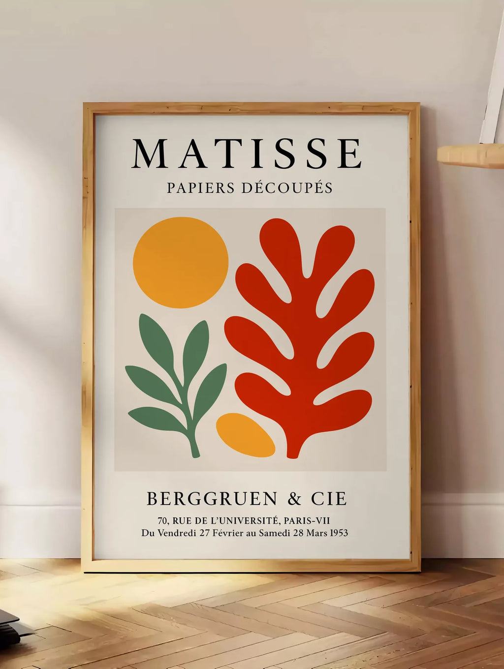 Estampe disque Branche et Corail Rouge en papiers decoupes Matisse sur fond colore, posee au sol dans un coin salon, sur un parquet a chevrons, pres d'une table d'appoint en chene chargee de livres