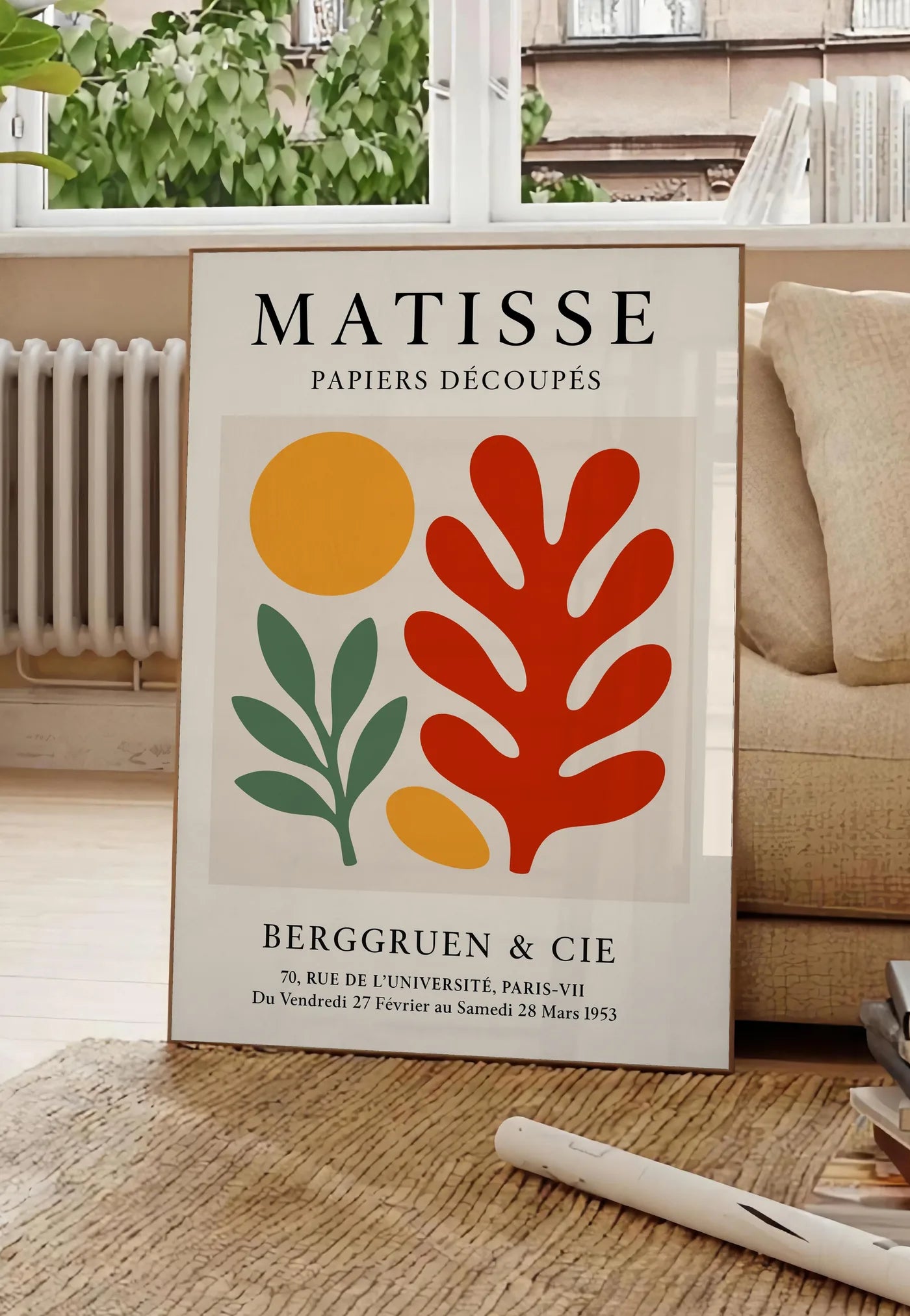 Poster disque Branche et Corail Rouge en papiers decoupes Matisse sur fond colore, posee au sol dans un salon parisien, devant une grande fenetre donnant sur un immeuble haussmannien, entre un ficus et un canape creme