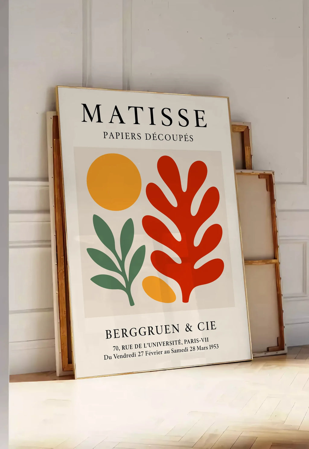 Tirage encadrable disque Branche et Corail Rouge en papiers decoupes Matisse sur fond colore, posee au sol dans une entree lumineuse, contre un mur a panneaux blancs, a cote de chassis en bois empiles