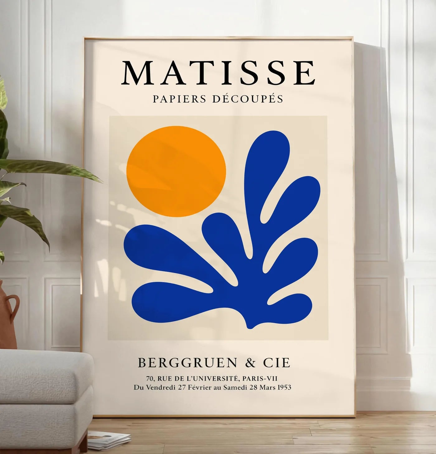 Reproduction soleil Orange et Corail Bleu en papiers decoupes Matisse sur fond colore, posee au sol dans un salon minimaliste clair, a cote d'un canape beige et d'une plante verte, sur un parquet clair