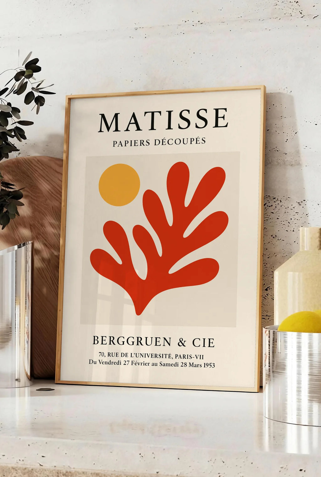Affiche soleil Orange et Corail Rouge en papiers decoupes Matisse sur fond colore, posee sur un plan de travail de cuisine en pierre claire, entre une branche d'eucalyptus en vase et un bocal de citrons