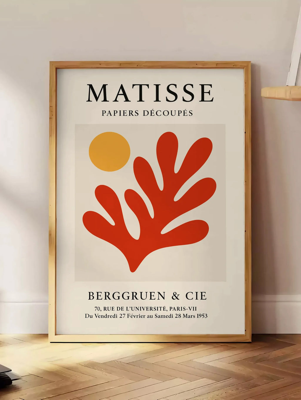 Estampe soleil Orange et Corail Rouge en papiers decoupes Matisse sur fond colore, posee au sol dans un coin salon, sur un parquet a chevrons, pres d'une table d'appoint en chene chargee de livres