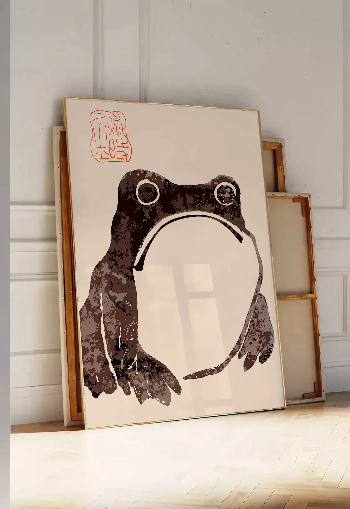 Tirage encadrable affiche grenouille blasee de Matsumoto Hoji, posee au sol dans une entree lumineuse, contre un mur a panneaux blancs, a cote de chassis en bois empiles