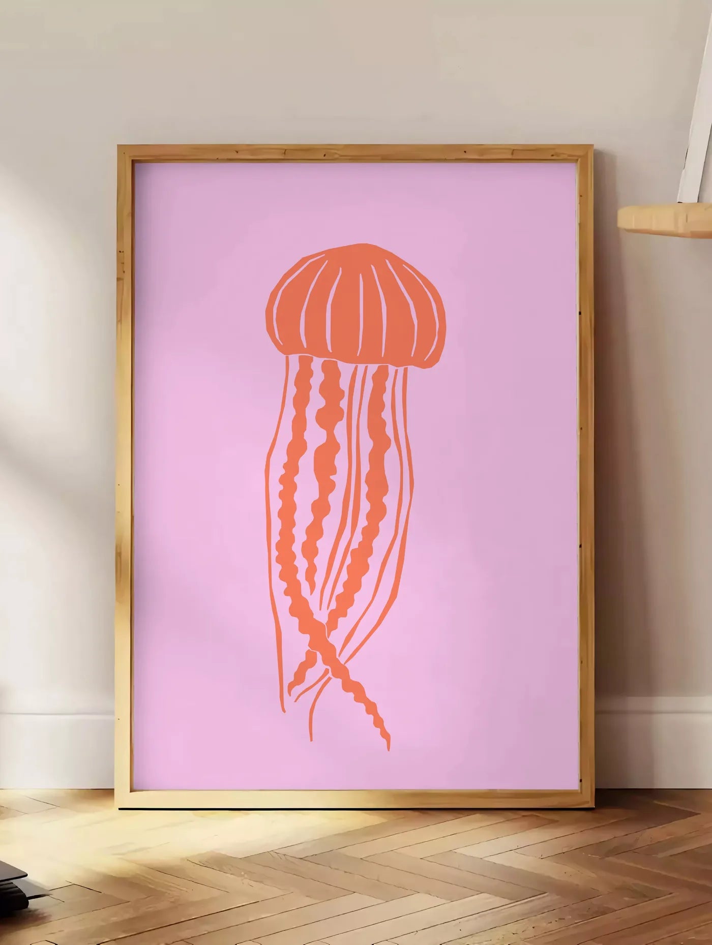 Estampe affiche meduse minimaliste, posee au sol dans un coin salon, sur un parquet a chevrons, pres d'une table d'appoint en chene chargee de livres