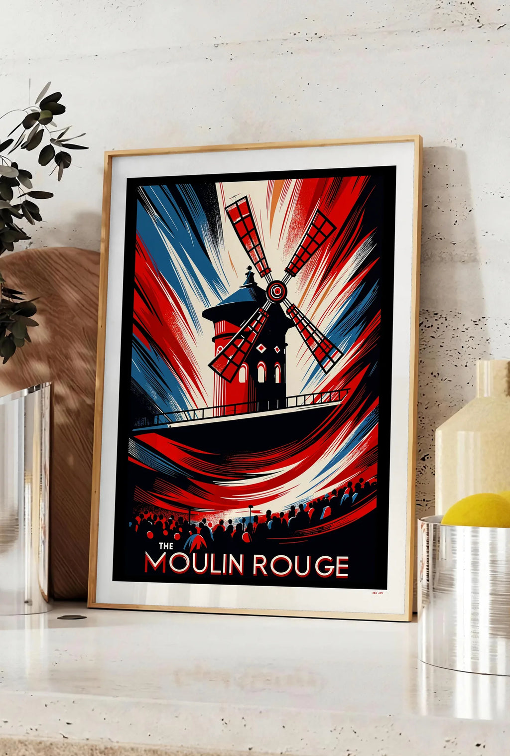 Affiche affiche Moulin Rouge Art Deco, posee sur un plan de travail de cuisine en pierre claire, entre une branche d'eucalyptus en vase et un bocal de citrons