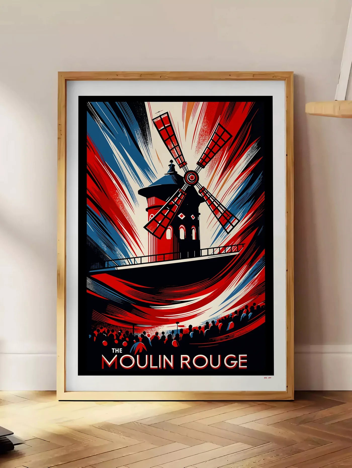 Estampe affiche Moulin Rouge Art Deco, posee au sol dans un coin salon, sur un parquet a chevrons, pres d'une table d'appoint en chene chargee de livres