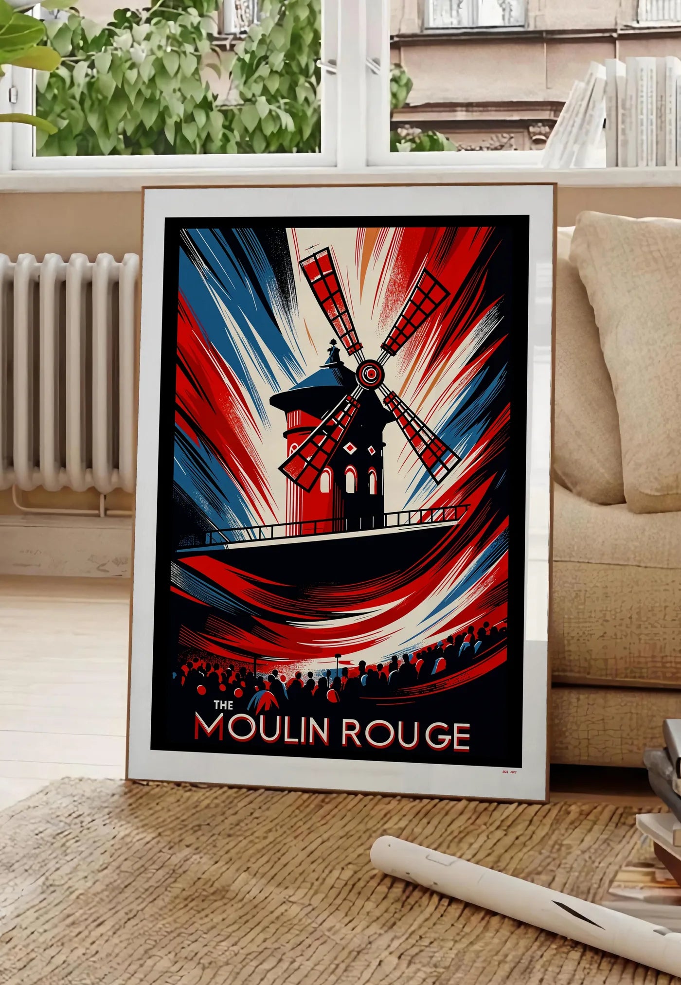Poster affiche Moulin Rouge Art Deco, posee au sol dans un salon parisien, devant une grande fenetre donnant sur un immeuble haussmannien, entre un ficus et un canape creme